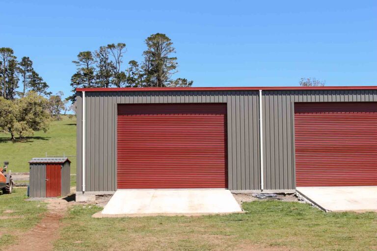 TechSpan steel farm shed with dark grey cladding and large red roller doors on a green rural hillside property