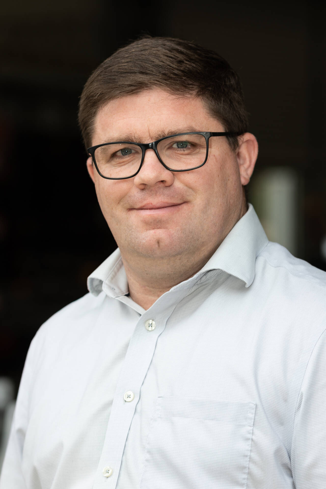 Portrait of Daniel Sanderson from TechSpan Building Systems standing in a workshop environment wearing glasses and a light business shirt.