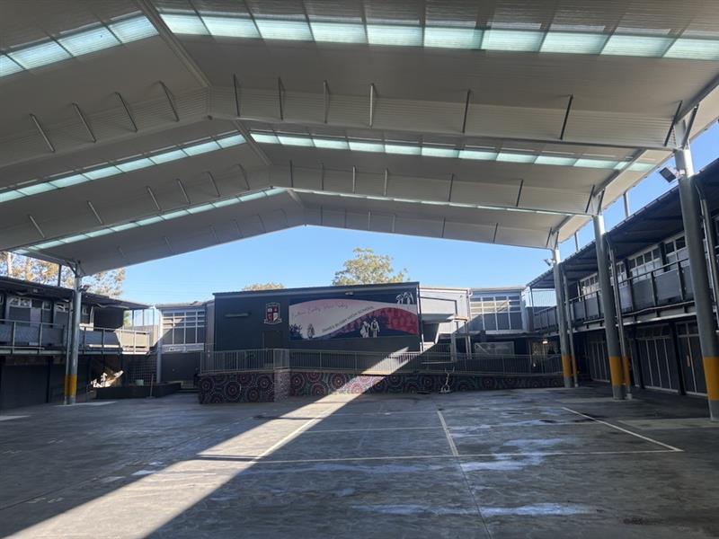 View from beneath a large school COLA showing the clear-span steel structure, translucent roof panels and open quadrangle space below.