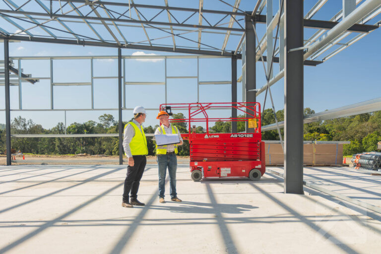 Builder and construction professional reviewing plans inside a large steel building under construction
